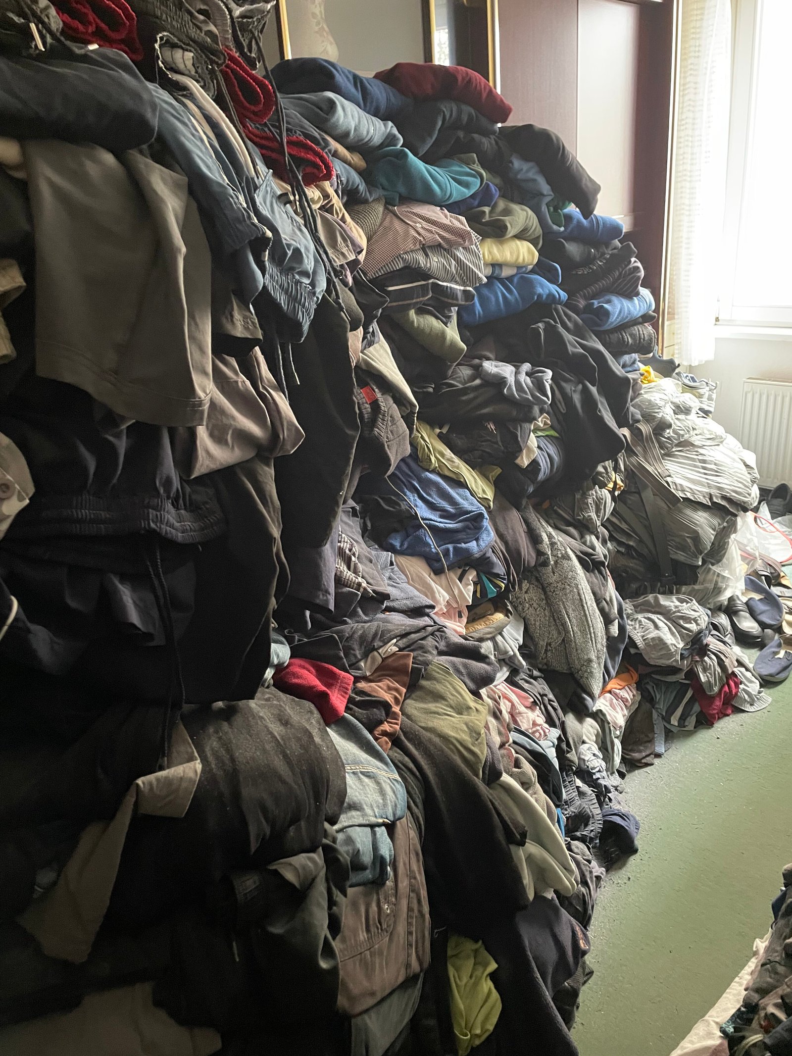 Messiewohnung Typ 2 mit hohen Kleiderstapeln und schmalem Laufgang